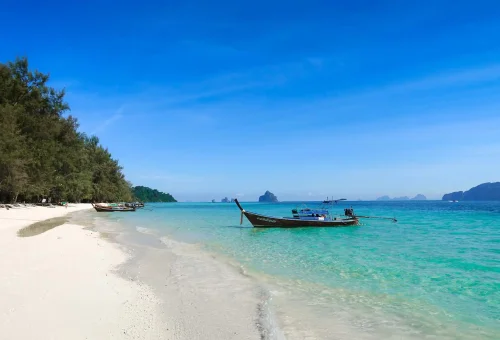 Traditional Thai longtail boat anchored on the white sandy beach of Koh Kradan with clear turquoise waters and a tropical backdrop