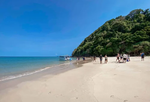 Tourists stepping off a boat onto the white sandy beach of Koh Kradan, surrounded by clear turquoise water and tropical scenery