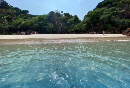 Visitors relaxing on Koh Kradan’s white sand beach with clear blue skies and calm turquoise waters in the background