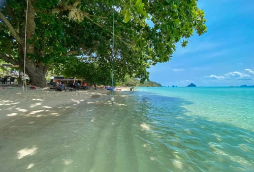 Relaxed beach scene on Koh Kradan with people sunbathing, swimming, and enjoying the clear blue sea and white sand