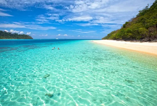 Scenic view of Koh Rok beach with soft white sand, clear turquoise water, and lush greenery in the background
