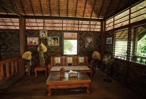 Traditional wooden Thai house at Old Phuket Farm, surrounded by tropical plants and reflecting classic rural architecture