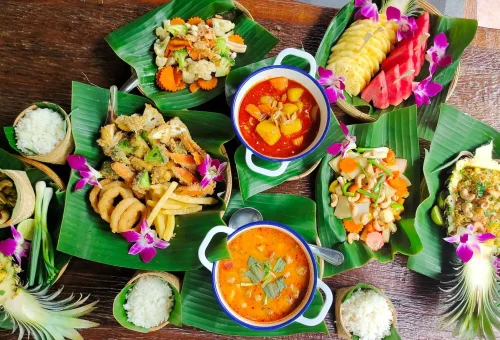 Guests preparing Thai dishes during a cooking class at Old Phuket Farm, surrounded by traditional kitchenware and a tropical garden