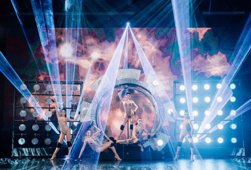 Simon Cabaret Phuket performer in a glamorous costume on stage with colorful lighting and theatrical backdrop.