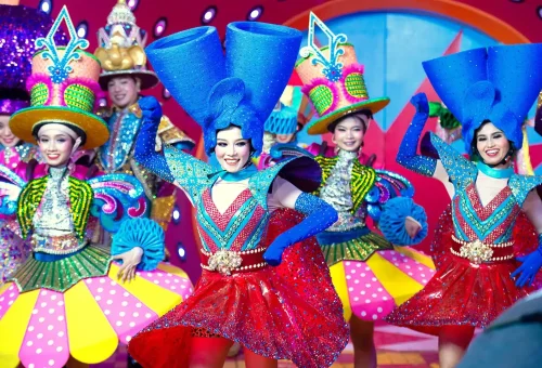 Performers in elaborate costumes dancing under glowing lights at Carnival Magic Phuket