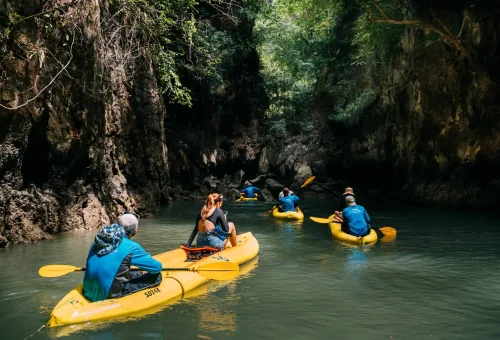 Visitors canoeing into a peaceful lagoon surrounded by towering cliffs at dusk, Hong Island by Starlight