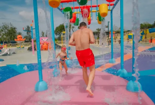 Kids running through a colorful water tunnel with cascading showers at Andamanda Phuket Waterpark, laughing and playing.
