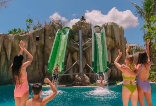 Thrill-seekers zooming down high-speed, multi-lane water slides at Andamanda Phuket Waterpark, surrounded by vibrant tropical décor.
