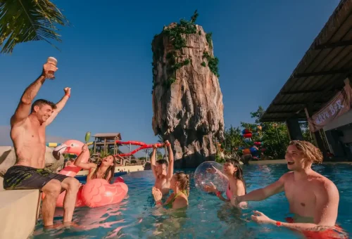 Smiling visitors splashing and playing in the large, crystal-clear pool at Andamanda Phuket Waterpark on a sunny day.