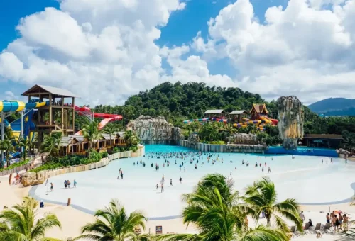 Aerial view of Andamanda Phuket Waterpark showcasing expansive pools, colorful slides, lush landscaping, and themed zones under blue skies.