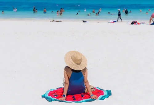 A pristine white sandy beach at Phi Phi Islands with gentle turquoise waves, palm trees, and a speed catamaran anchored nearby under a clear blue sky.