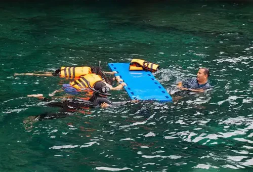 A happy customer snorkeling in the clear, tropical waters of Phi Phi Islands, surrounded by coral reefs and colorful fish, with a speed catamaran in the background.