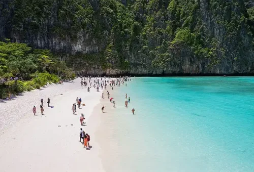 Breathtaking panoramic view of Maya Bay at Phi Phi Islands, featuring emerald waters, lush cliffs, and a speed catamaran anchored offshore.
