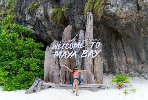 Tourists stepping off a speed catamaran onto the shore of Maya Bay at Phi Phi Islands, greeted by crystal-clear waters and lush cliffs.