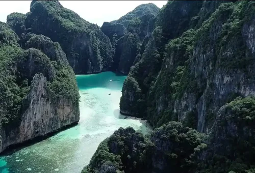 Aerial view of Pileh Lagoon at Phi Phi Islands, showcasing crystal-clear emerald water surrounded by towering limestone cliffs and a speed catamaran floating below.