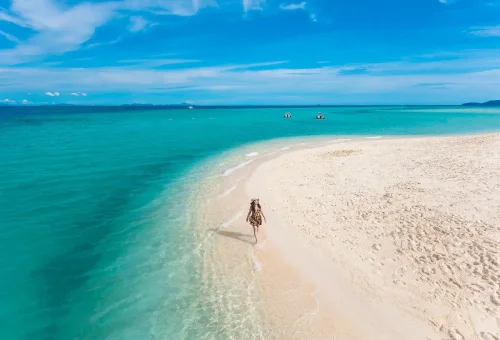 Aerial view of the white sandy beach at Bamboo Island near Phi Phi, featuring turquoise waters, lush green edges, and a speed catamaran anchored offshore.