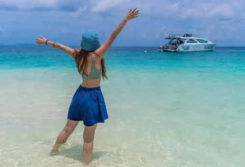 View of the white sandy beach at Bamboo Island with a sleek speed catamaran anchored nearby, turquoise waters gently lapping the shore.