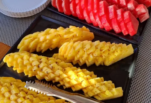 A colorful tray of fresh tropical fruits served on board a speed catamaran, with the turquoise waters of Phi Phi Islands in the background.