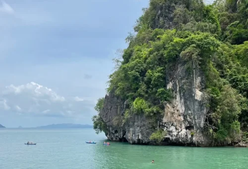 A guest canoeing through calm waters and limestone caves at Panak Island with Andaman Sea Kayak, surrounded by dramatic rock formations and lush greenery.