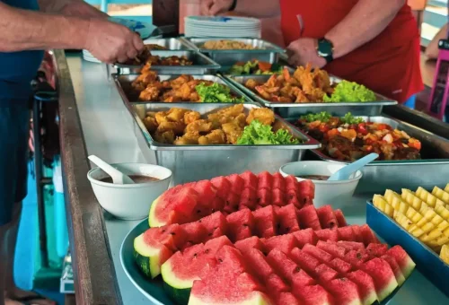 A colorful Thai lunch buffet served on board during the Andaman Sea Kayak tour, featuring rice dishes, curries, fruits, and refreshing drinks with sea views.