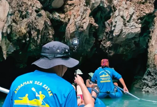 Customers paddling a canoe through a narrow sea cave with Andaman Sea Kayak, surrounded by dramatic limestone formations and calm emerald waters.