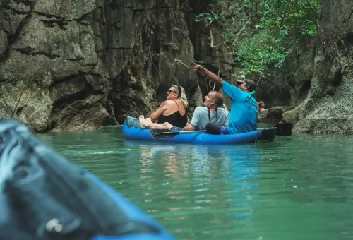 Andaman Sea Kayak paddle guides navigating through a peaceful lagoon surrounded by towering limestone cliffs and tropical vegetation.