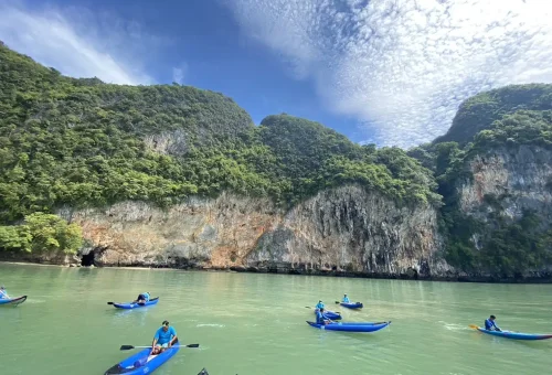 Andaman Sea Kayak paddle guides gently paddling through a shadowy limestone cave, surrounded by calm, reflective waters and dramatic cave walls.