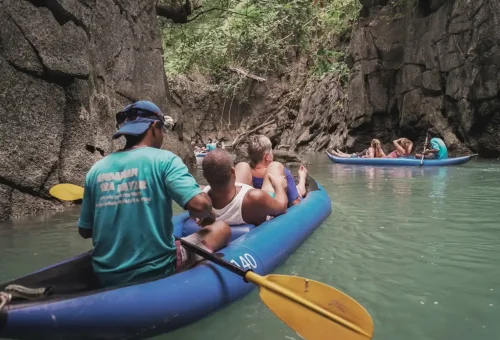 A canoe entering a limestone cave with low-hanging rock formations and calm, reflective water during an Andaman Sea Kayak adventure.