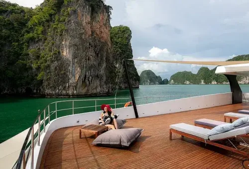 A woman relaxing on the sundeck of a luxury catamaran near James Bond Island, enjoying the sunshine and panoramic ocean views.