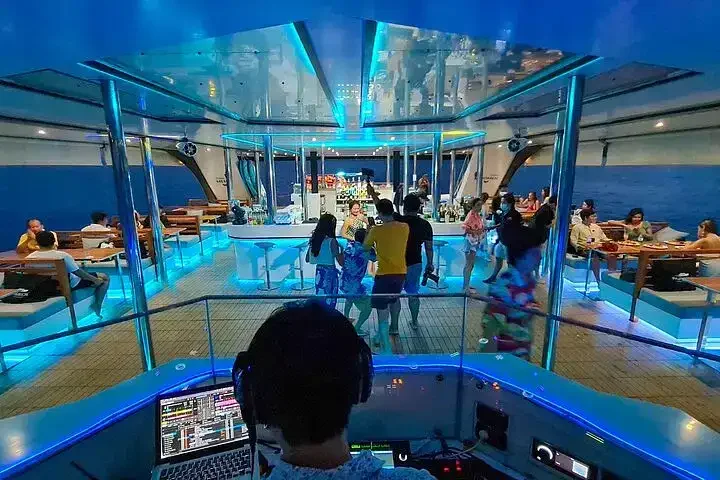 A DJ playing upbeat music on the deck of a luxury catamaran near James Bond Island, with party vibes and ocean views all around.