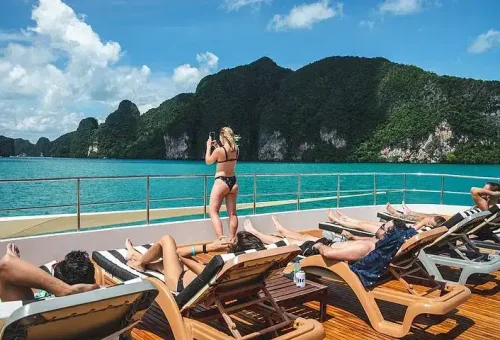 Guest's lounging on a sunbed aboard a luxury catamaran, enjoying the panoramic ocean view and coastal cliffs near James Bond Island.
