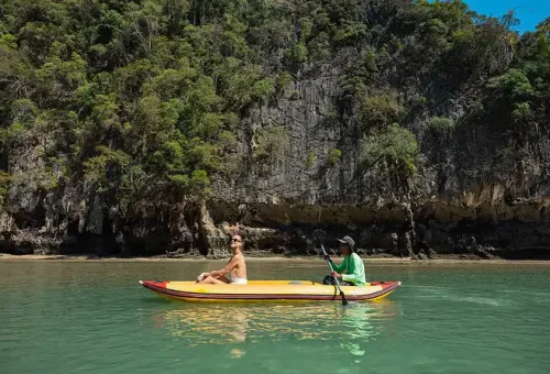 A guided canoe paddling along the dramatic limestone cliffs of Panak Island, with guests enjoying the tranquil waters near a luxury catamaran.