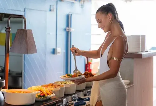 A woman enjoying a vibrant buffet spread on the deck of a party boat in Phang Nga Bay, with a variety of dishes and ocean views in the background.