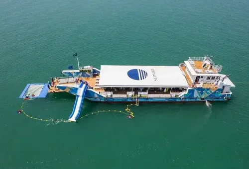 Aerial view of a lively party boat cruising through the emerald waters of Phang Nga Bay, surrounded by dramatic limestone cliffs and scenic islands.