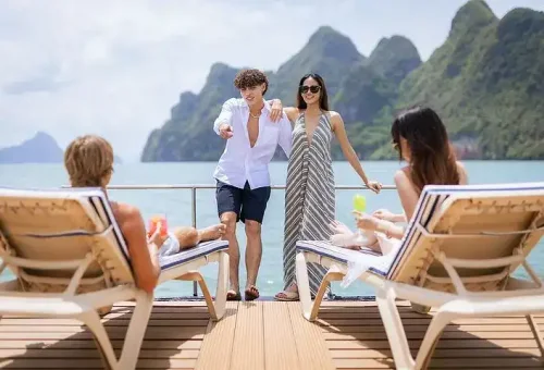 Guests relaxing and sunbathing on the sundeck of a party boat cruising through Phang Nga Bay, surrounded by clear skies and stunning sea views.