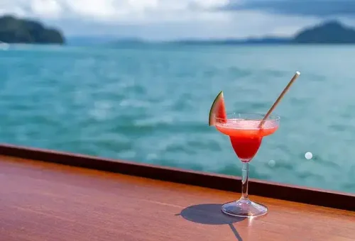 Guests enjoying colorful cocktails on the deck of a party boat during the Phang Nga Bay cruise, with scenic ocean views and a lively atmosphere.