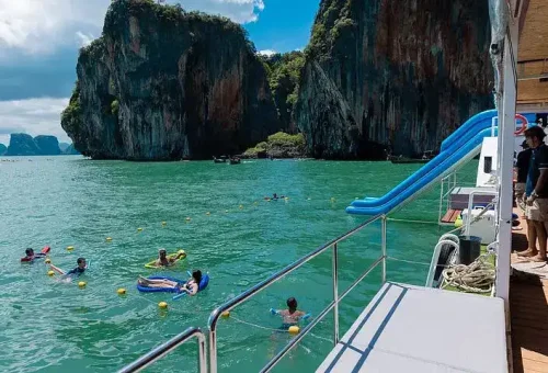 Happy customer swimming in the clear turquoise waters in front of Hong Island, with the party boat anchored nearby and limestone cliffs in the background.