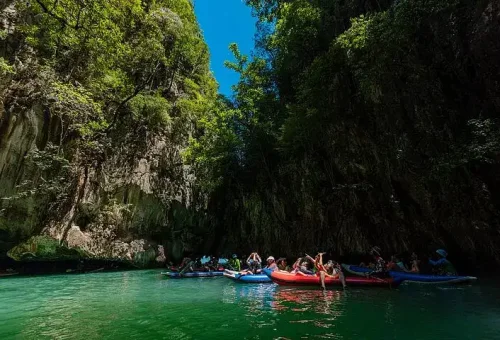 Guests enjoying sea cave canoeing at Hong Island, gliding through emerald waters beneath towering limestone cliffs during the Phang Nga Bay Party Cruise.