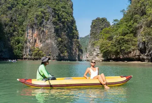A guided canoe gliding through a sea cave at Hong Island, with guests enjoying the calm waters and dramatic limestone surroundings during the Phang Nga Bay Party Cruise.