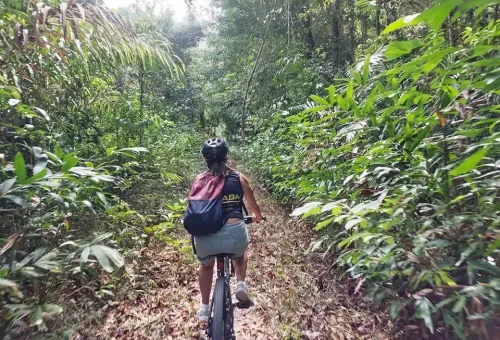 Cyclist at a rural crossroads in Phuket, choosing between jungle trails and village paths, surrounded by tropical greenery and open skies.