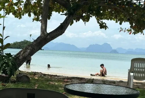 Traveler relaxing on a quiet sandy beach at Koh Yao Noi, with clear blue waters, gentle waves, and a backdrop of tropical islands.