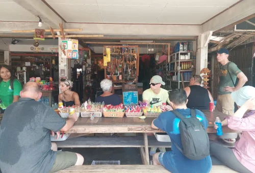 Cycling group resting at a small local shop on Koh Yao Noi, enjoying drinks and snacks under a shaded area in a quiet village setting.