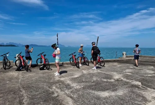 Cyclist resting at a wooden pier on Koh Yao Noi, overlooking calm turquoise waters and distant islands under a bright tropical sky.