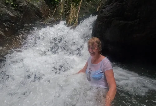 Customers joyfully playing in the water at a jungle waterfall in Phuket’s rainforest, surrounded by lush tropical greenery and natural rock pools.