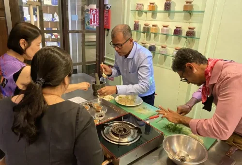Students focused and actively cooking Thai dishes in the kitchen at Blue Elephant Cooking School in Phuket.