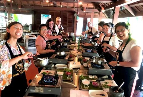 Group of cooking students gathered at the stoves, actively preparing Thai dishes during a hands-on session at Blue Elephant Cooking School Phuket.