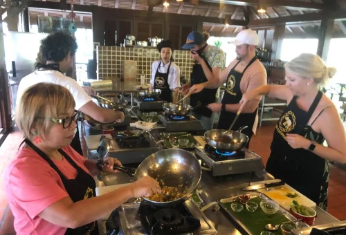 Students actively chopping, stirring, and cooking Thai dishes during a hands-on session at Blue Elephant Cooking School in Phuket.