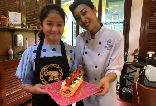 Group of smiling teenage students enjoying their cooking class at Blue Elephant Cooking School in Phuket, proudly showing their Thai dishes.