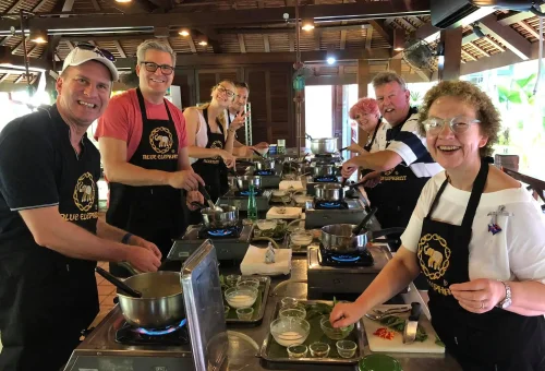 Joyful group of international tourist students posing with their freshly cooked Thai dishes at Blue Elephant Cooking School in Phuket.