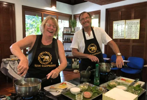 Enthusiastic students smiling and cooking together in the kitchen at Blue Elephant Cooking School Phuket, enjoying their Thai culinary class.
